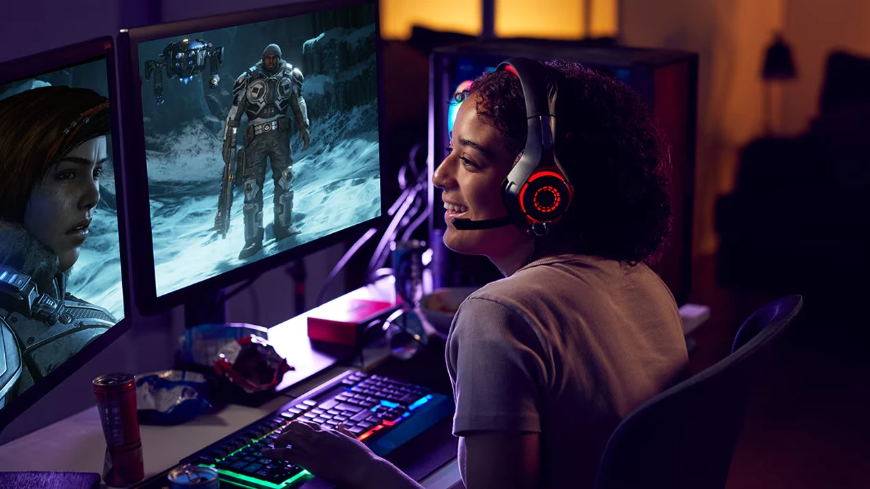 Gamerin mit Headset spielt auf Dual-Monitor-Setup, betrieben von einem Mini PC Windows 11 – flüssiges Gaming mit starker Performance und RGB-Beleuchtung